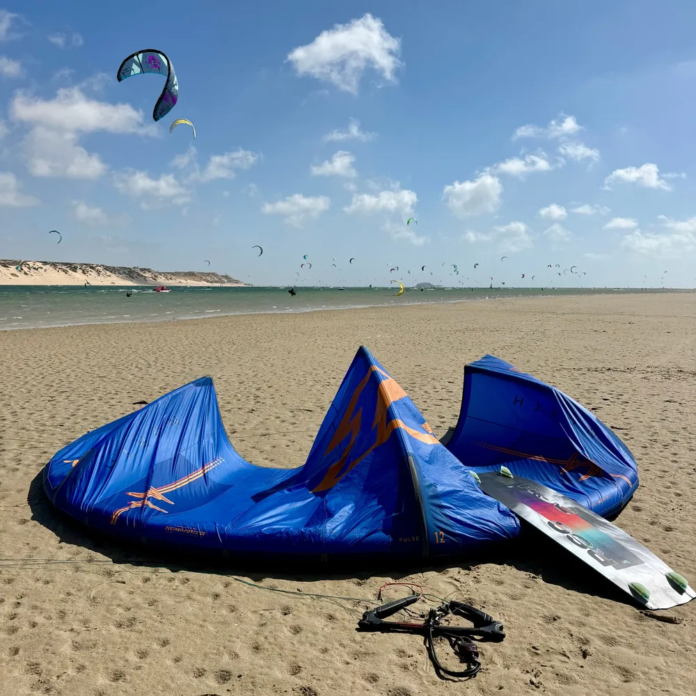 Aile de kitesurf bleue et planche posées sur le sable devant la lagune de Dakhla