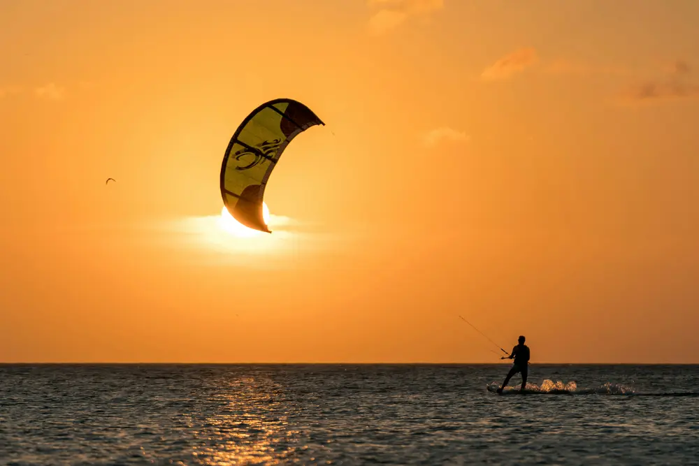 Kitesurfeur glissant au coucher du soleil, son aile de kitesurf en contre-jour devant le soleil