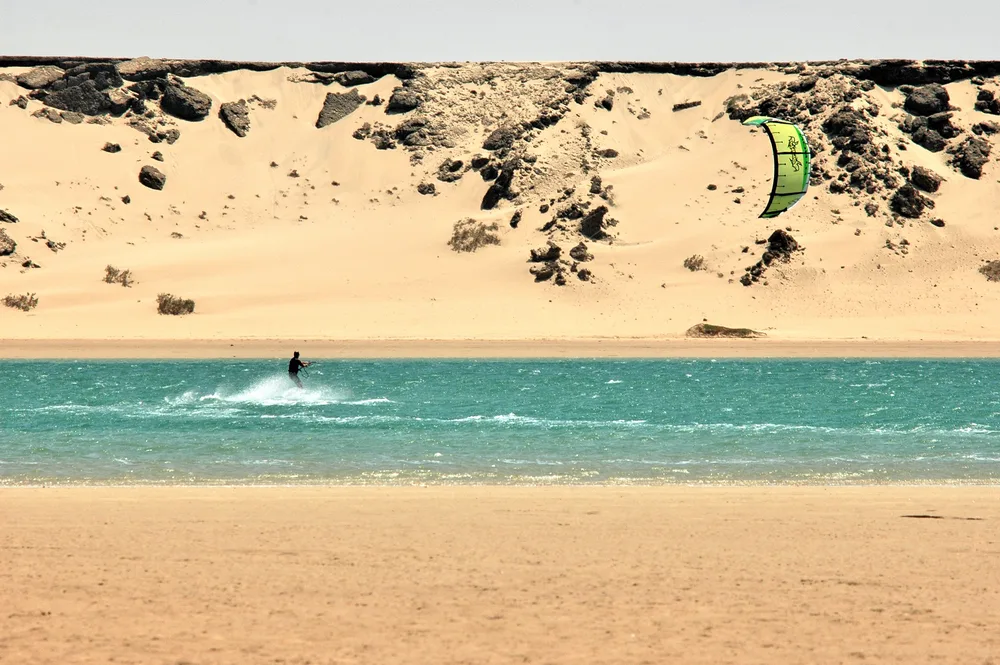 Kitesurfeur seul sur la lagune turquoise de Dakhla, falaises de sable en arrière plan