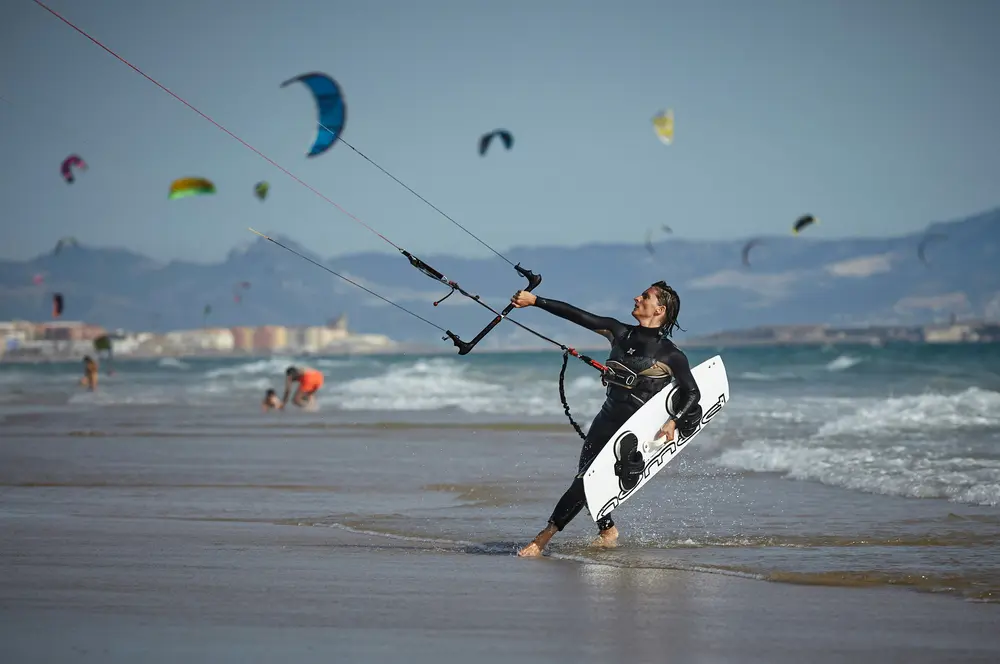 Kitesurfeuse sur la plage, planche sous le bras et barre en main avant la session
