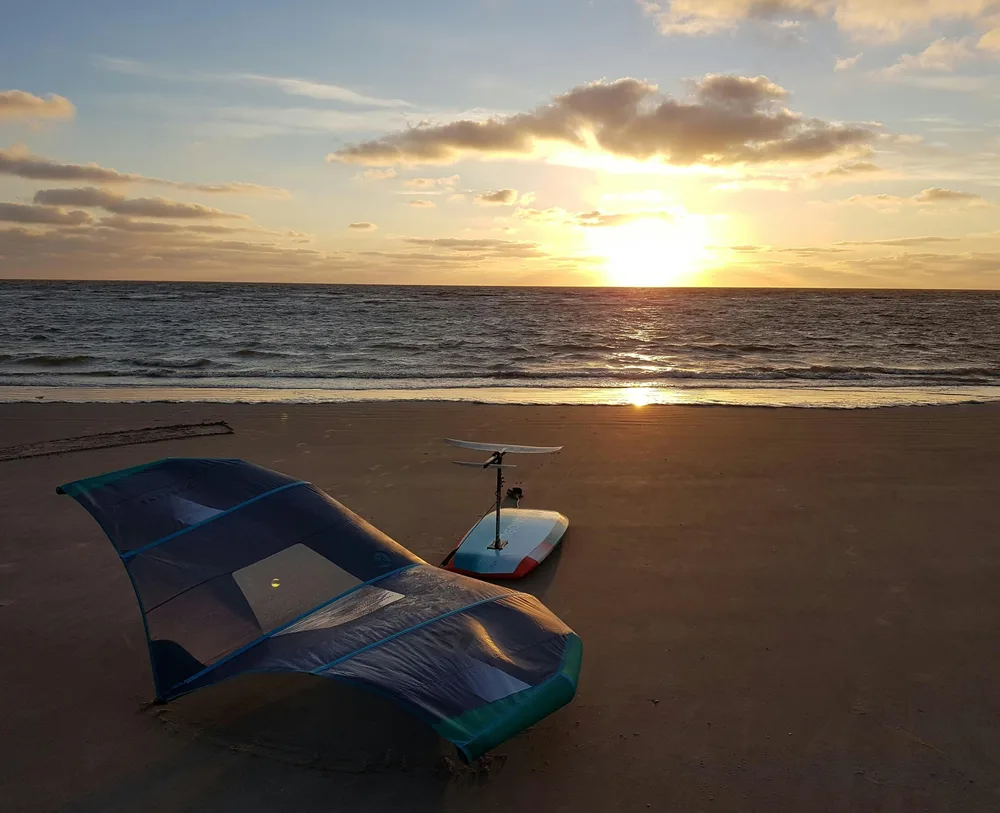 Matériel de wing foil posé sur la plage : aile gonflable, planche et foil