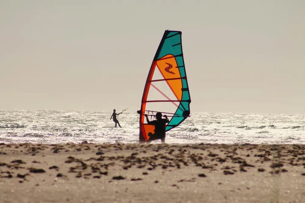 Gréement de windsurf au bord de la plage : voile, mât et wishbone prêts à la mise à l'eau