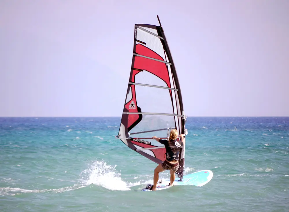 Windsurfeuse au planning sur une mer turquoise, voile rouge et blanche bien lisible