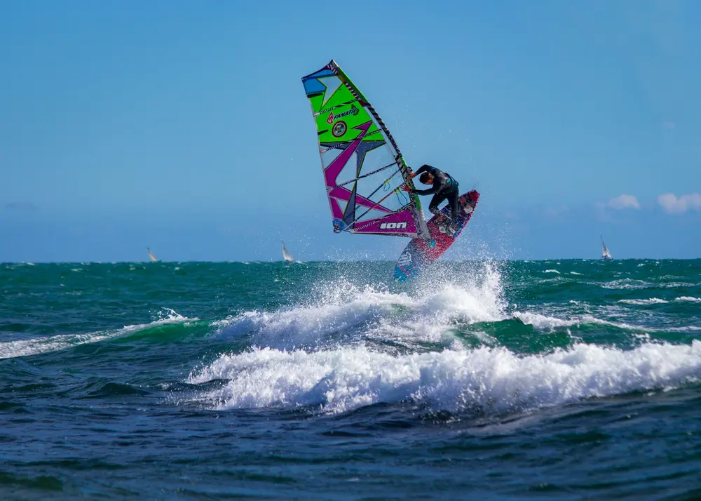 Windsurfeur déclenchant un saut au-dessus d'une vague, voile multicolore