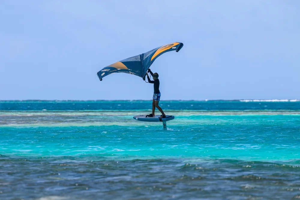 Wing foiler sur l'eau turquoise d'un lagon, aile orange et noire gonflée par le vent