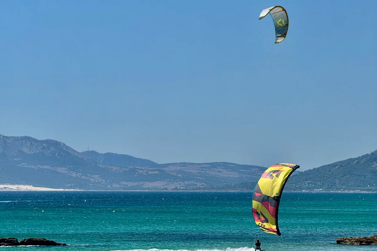 Kitesurfeur sur une vague à Tarifa, aile colorée et montagnes de Cádiz en fond