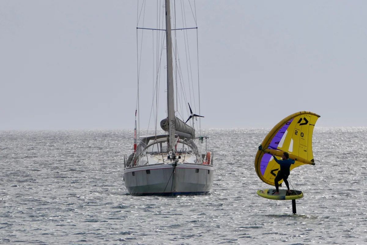 Wing foil près d'un voilier sur une eau calme en août